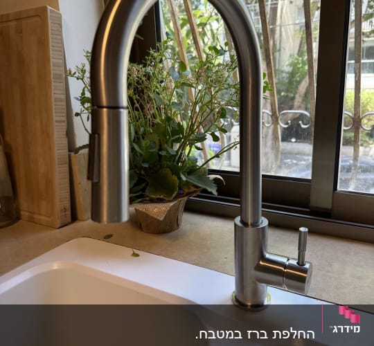 ברז נירוסטה מעל כיור במטבח ליד חלון